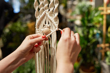 Load image into Gallery viewer, Details of Katie tying a knot in the process of making an Eye Spy macrameé wall hanging with white macramé rope.
