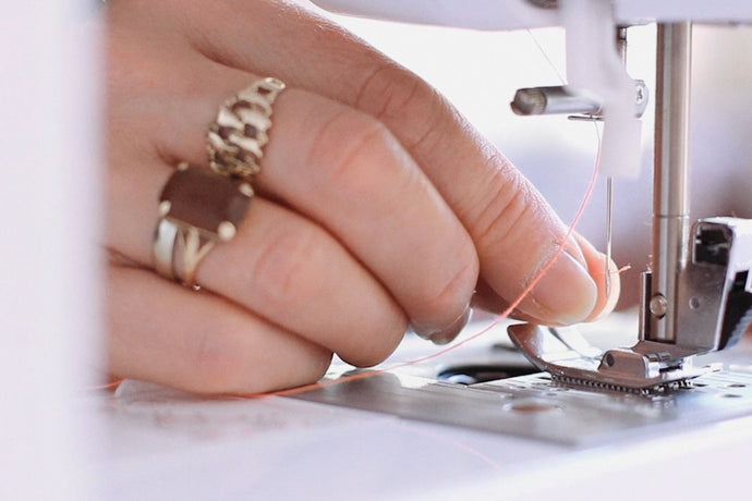 Close-up of hand feeding thread through sewing machine.