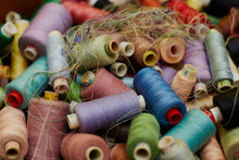Load image into Gallery viewer, A pile of colourful thread spools.
