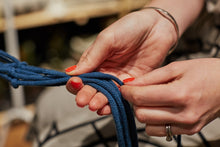 Load image into Gallery viewer, Close-up of two hands looping dark blue macramé cord.
