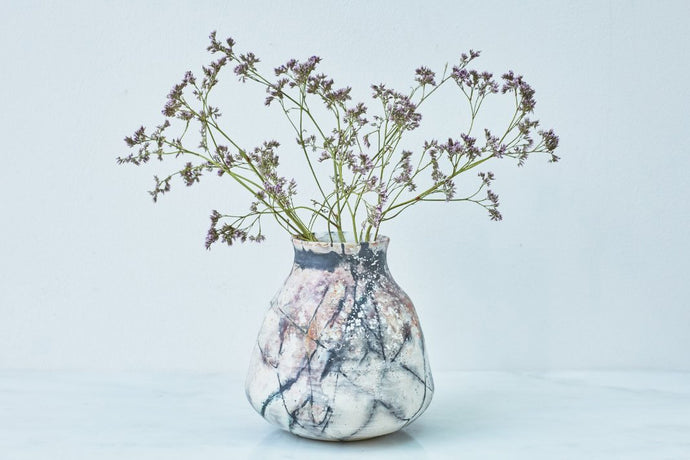 A smoke-fired ceramic vase with small purple flowers.